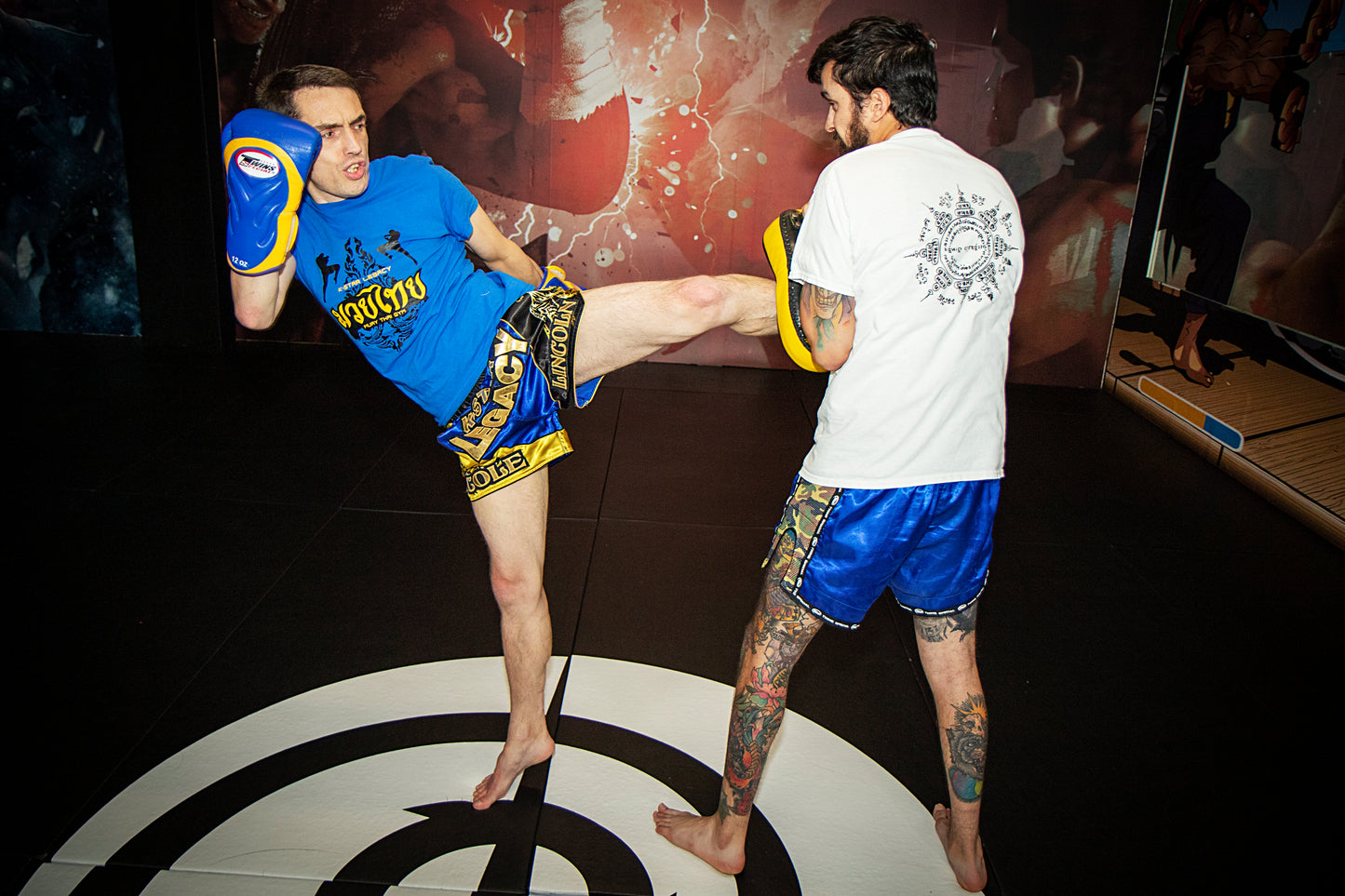 A photo of a fighter throwing kicks with a coach who is holding pads