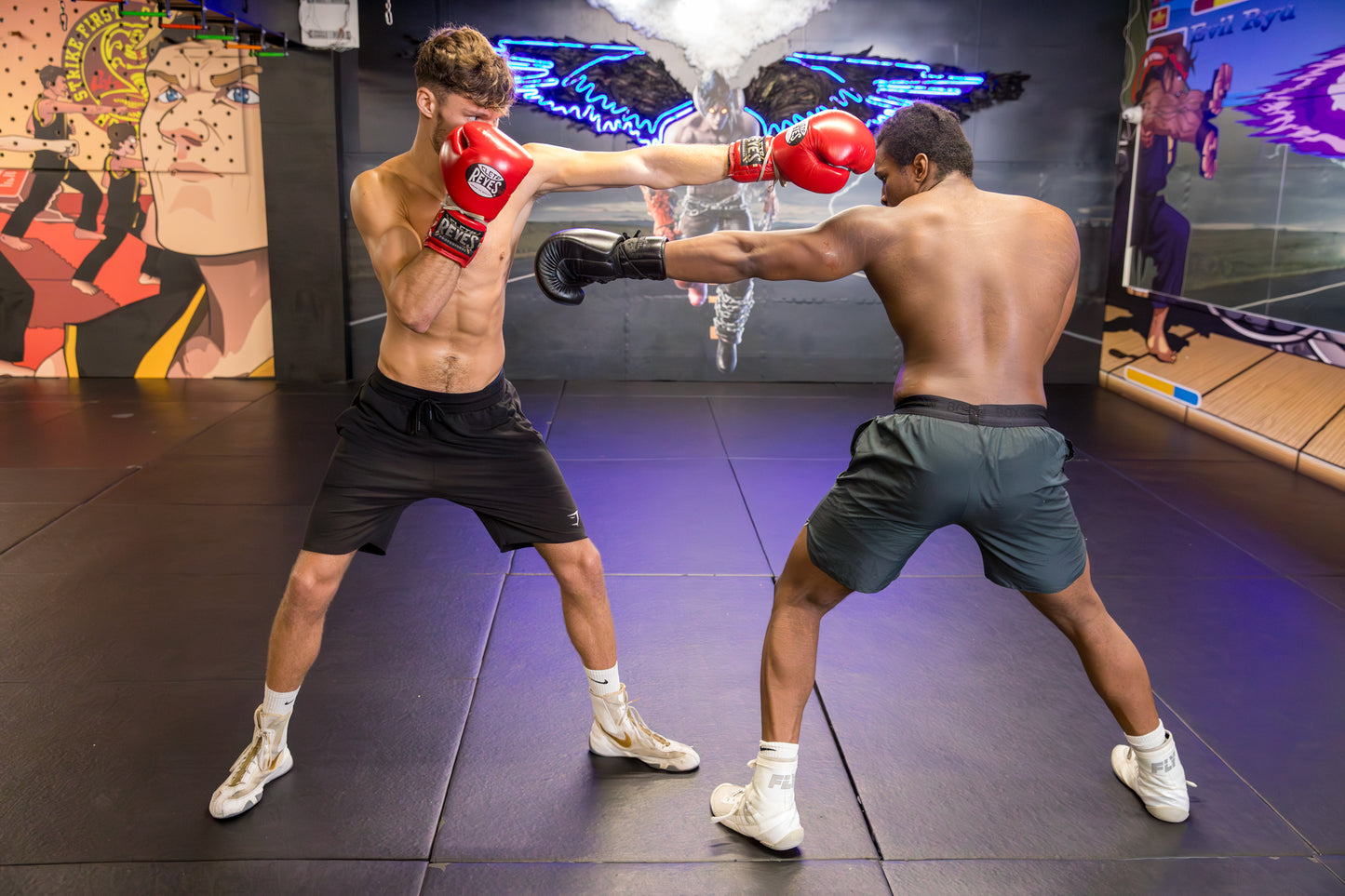 Two fighters training, one wearing red boxing gloves and black shorts, and the other wearing black gloves and dark green shorts, with a digital smoke effect in the centre of the background.