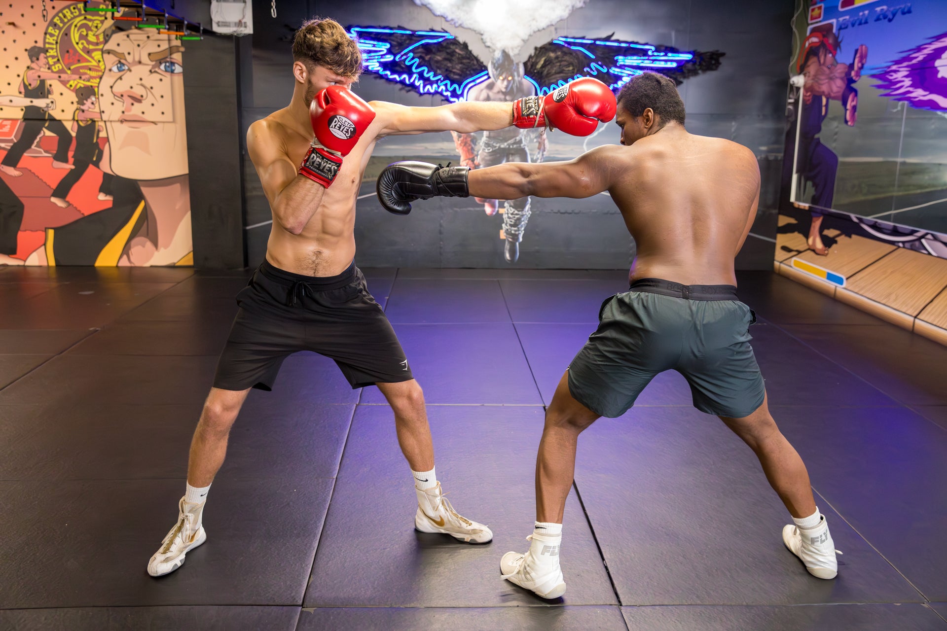 Two fighters training, one wearing red boxing gloves and black shorts, and the other wearing black gloves and dark green shorts, with a digital smoke effect in the centre of the background.