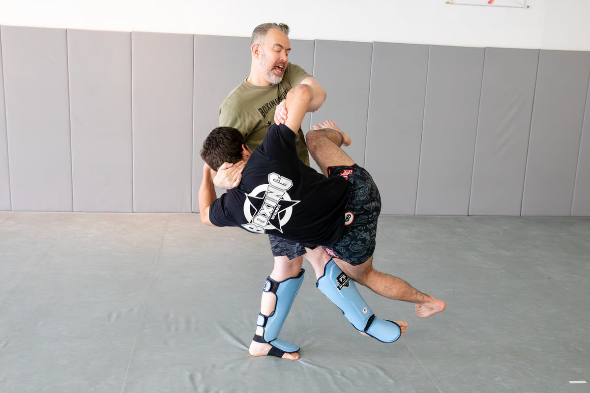A coach demonstrating how to perform a sweep on his fighter