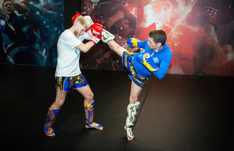 Two individuals in colorful martial arts uniforms practicing in front of a large screen displaying action sequences.