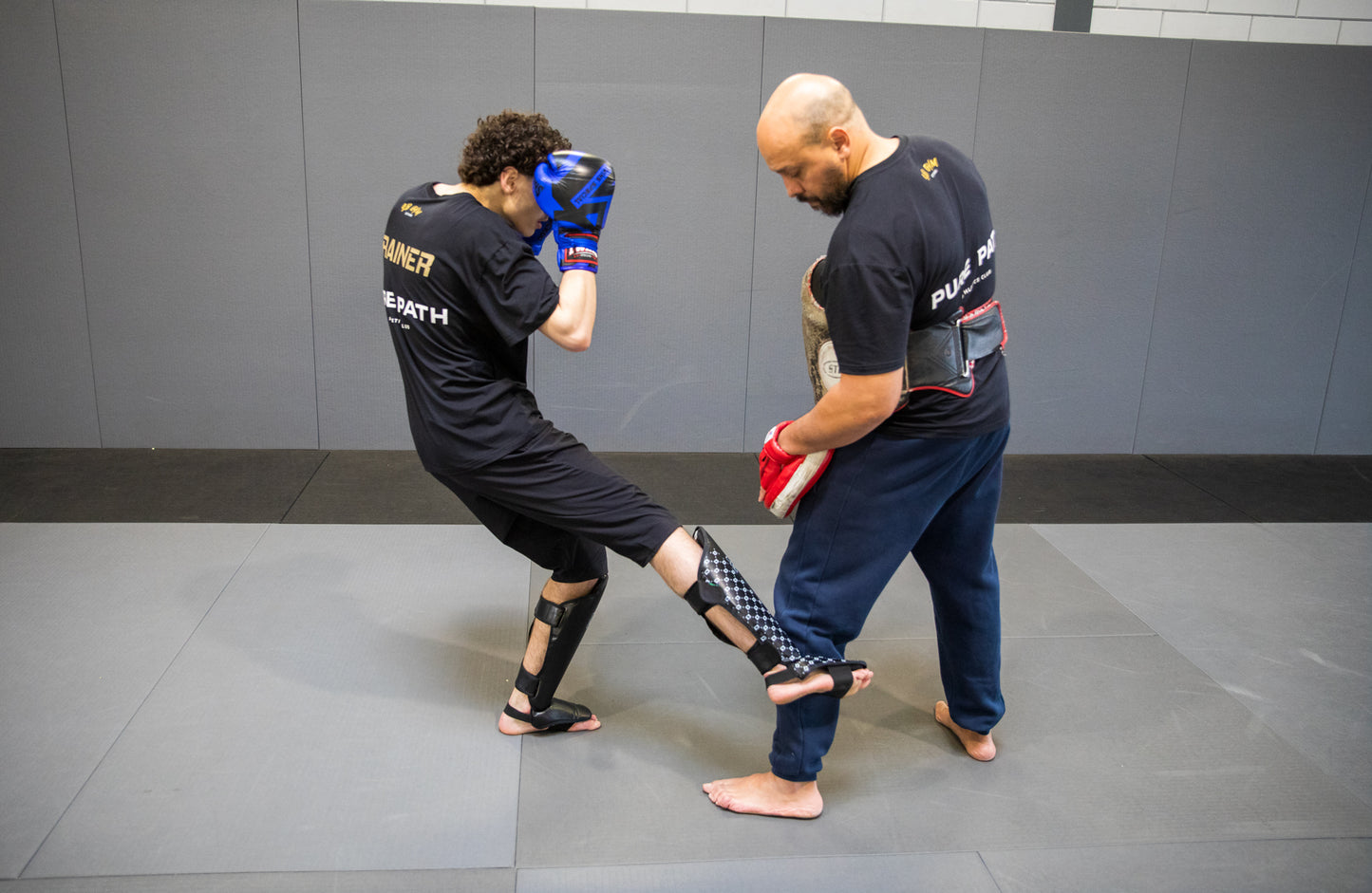 A fighter working kicks with his coach in a martial arts gym