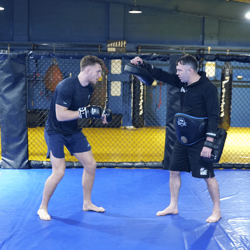 A GIF of a fighter demonstrating a jumping knee technique on the pads with his coach
