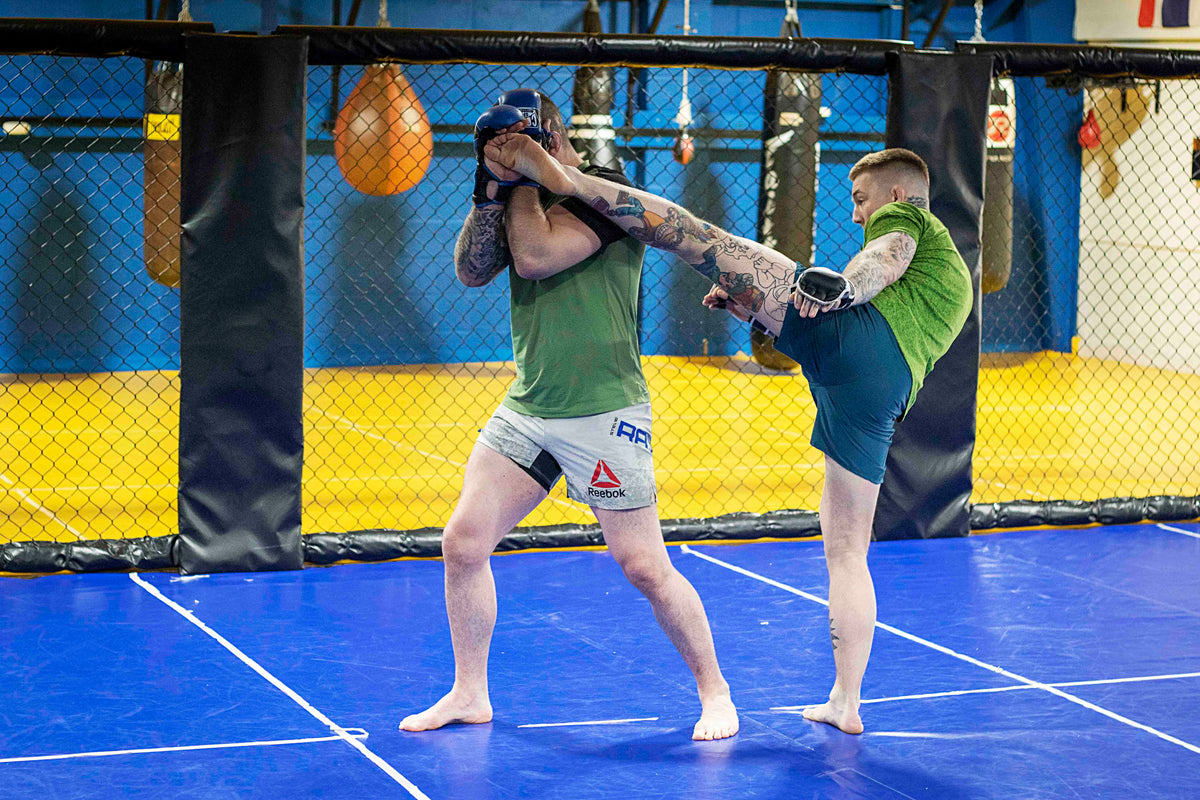 a fighter throwing a high kick at his training partner in a martial arts gym