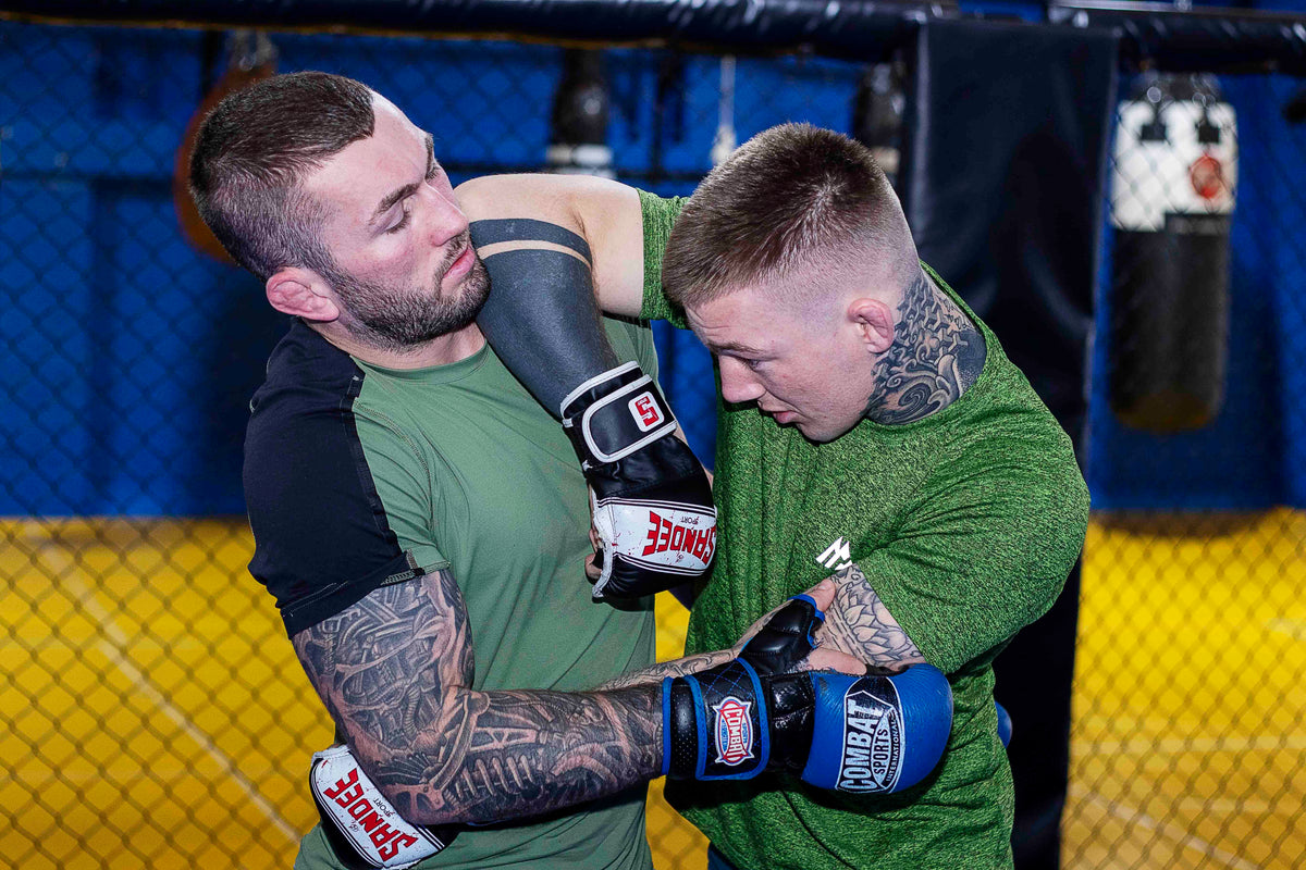 a fighter demonstrating an elbow strike from the clinch position whilst training his partner in a MMA gym