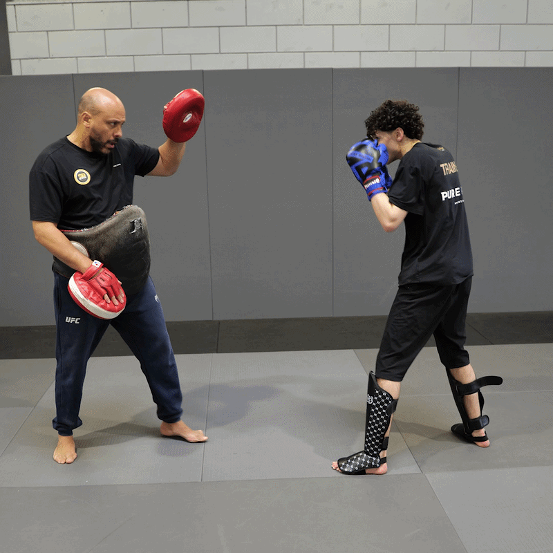 A coach training a fighter on the pads in a martial arts gym