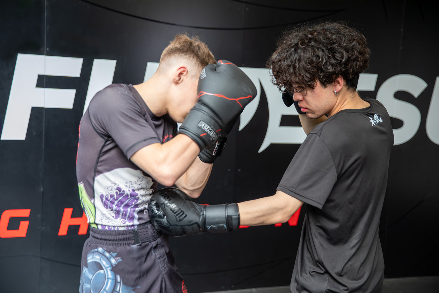 Two individuals in a martial arts training session with a branded backdrop