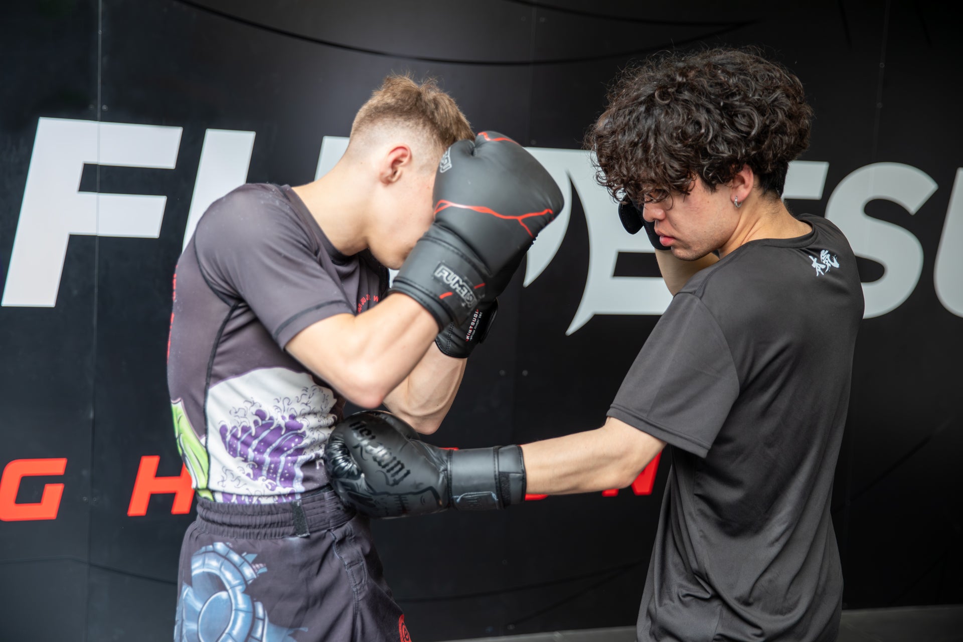 Two individuals in a martial arts training session with a branded backdrop