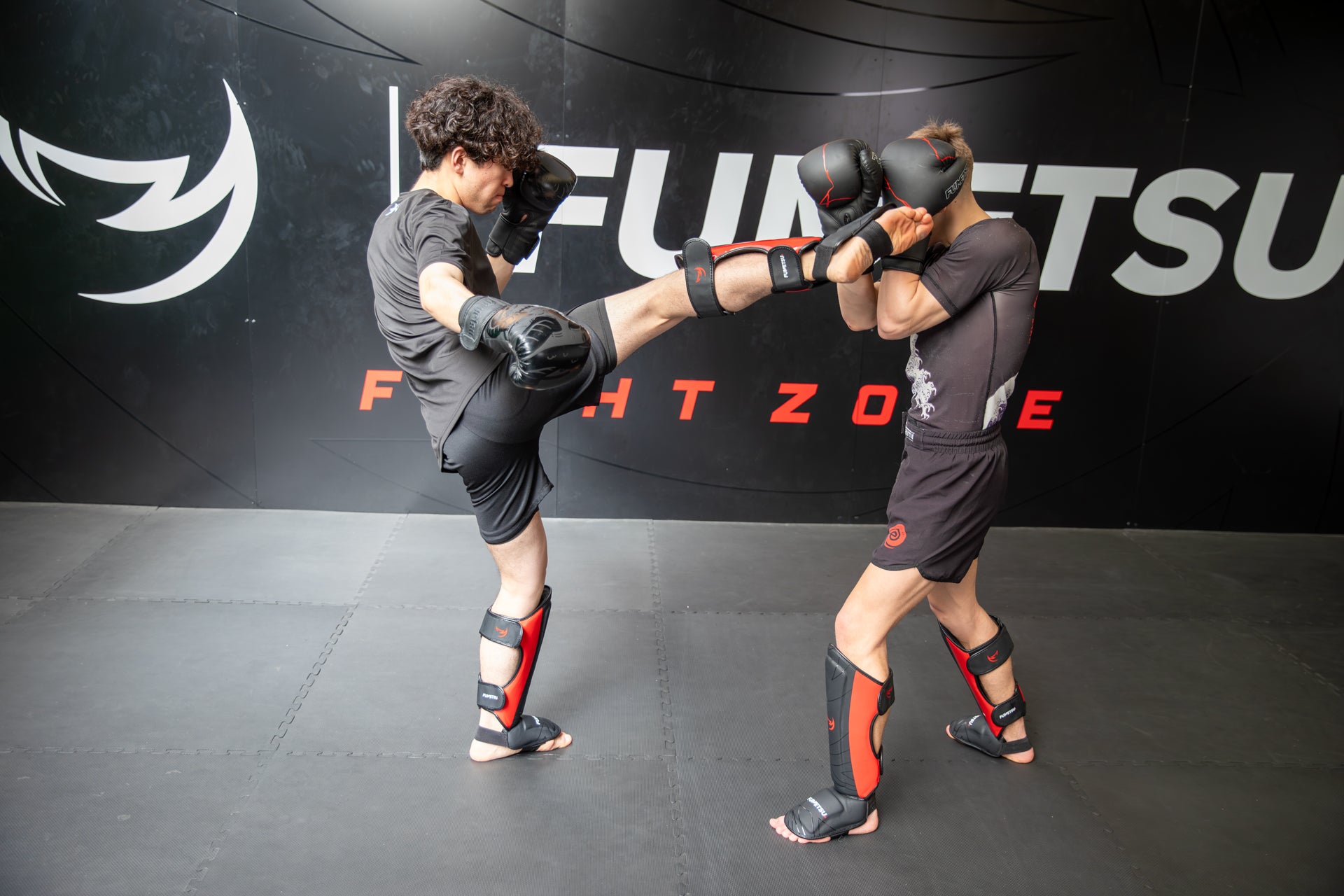 Two individuals practicing martial arts in a gym with 'Fumetsu Fight Zone' branding.