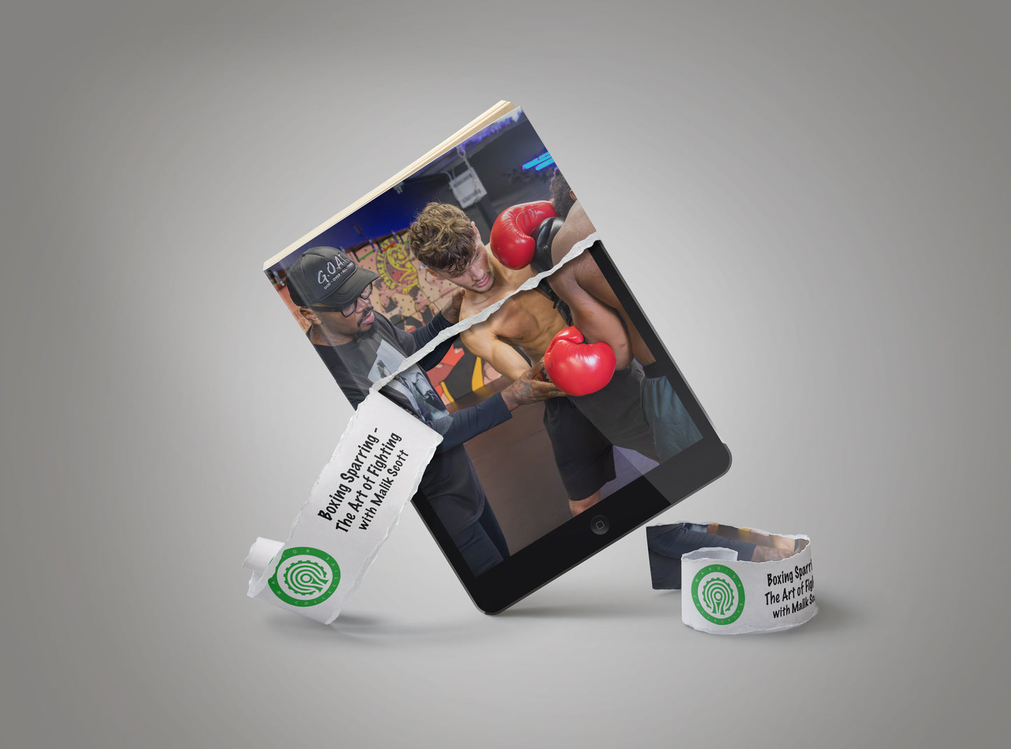 A black tablet and a torn-edge magazine or booklet are arranged on a gray studio background, with printed wristbands placed in front. The printed materials show boxing-themed imagery and text, including a green circular logo and a written phrase.