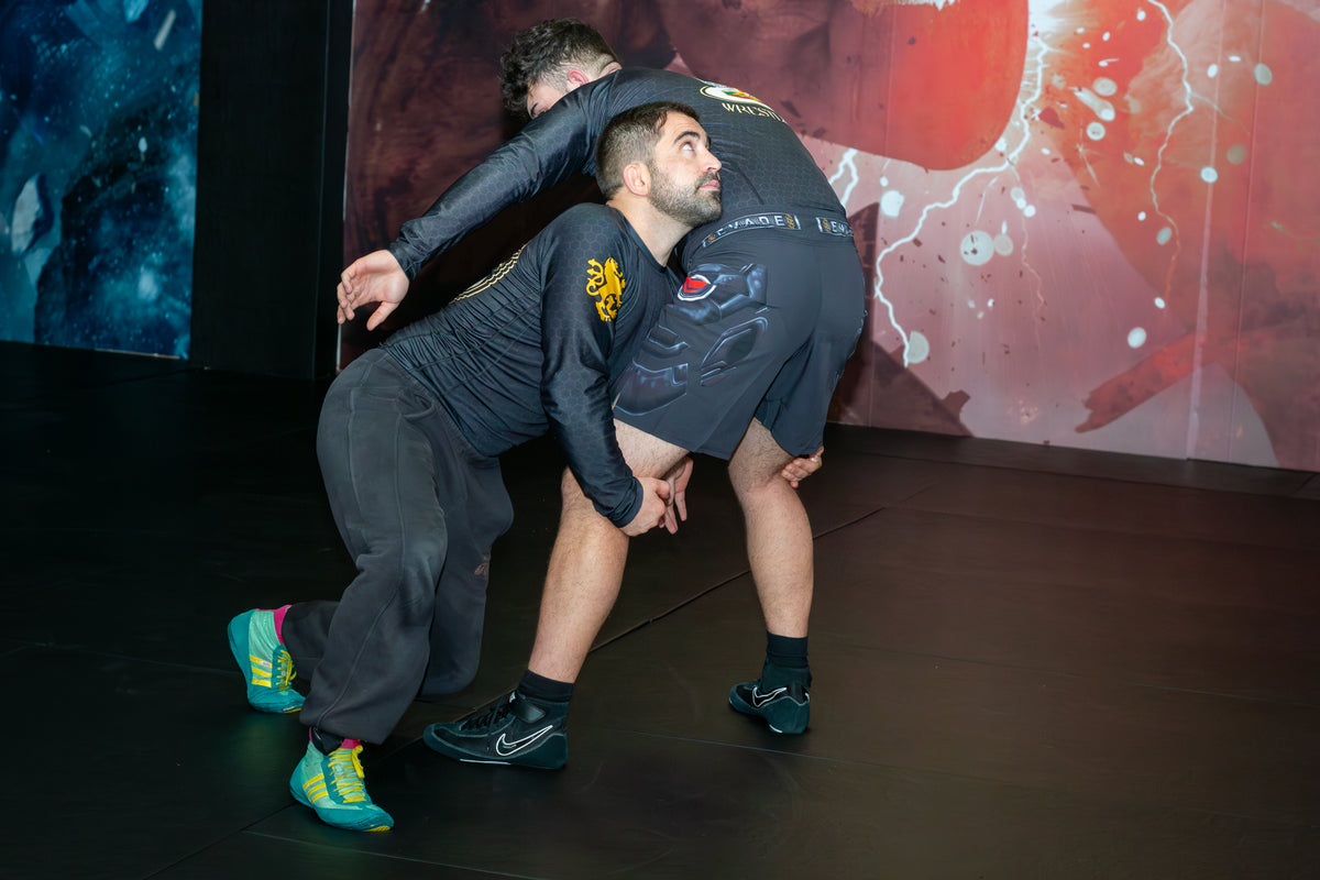 A wrestler demonstrating grappling drills with a partner on the mats in a martial arts gym