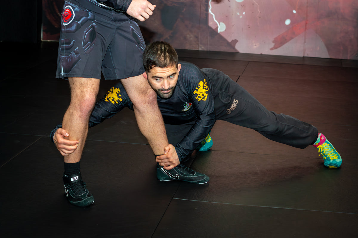 A wrestler demonstrating grappling drills with a partner on the mats in a martial arts gym