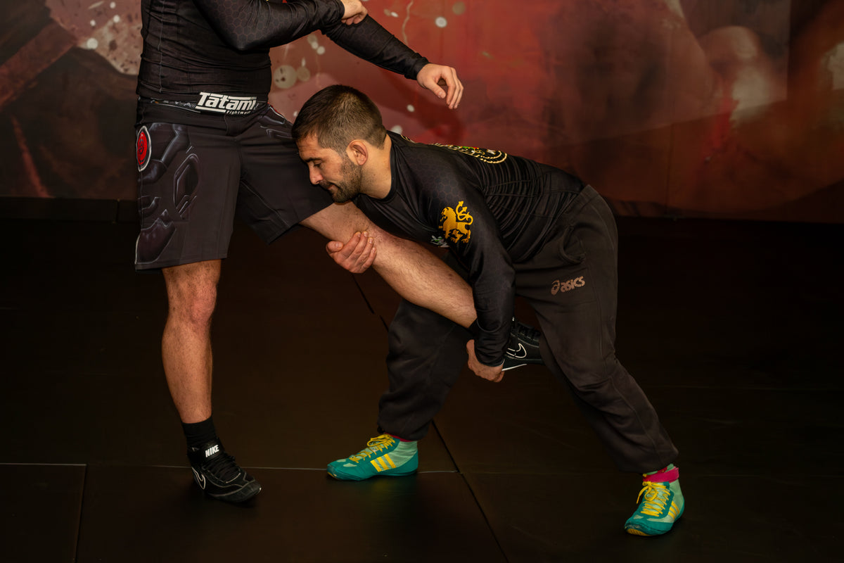 A wrestler demonstrating grappling drills with a partner on the mats in a martial arts gym