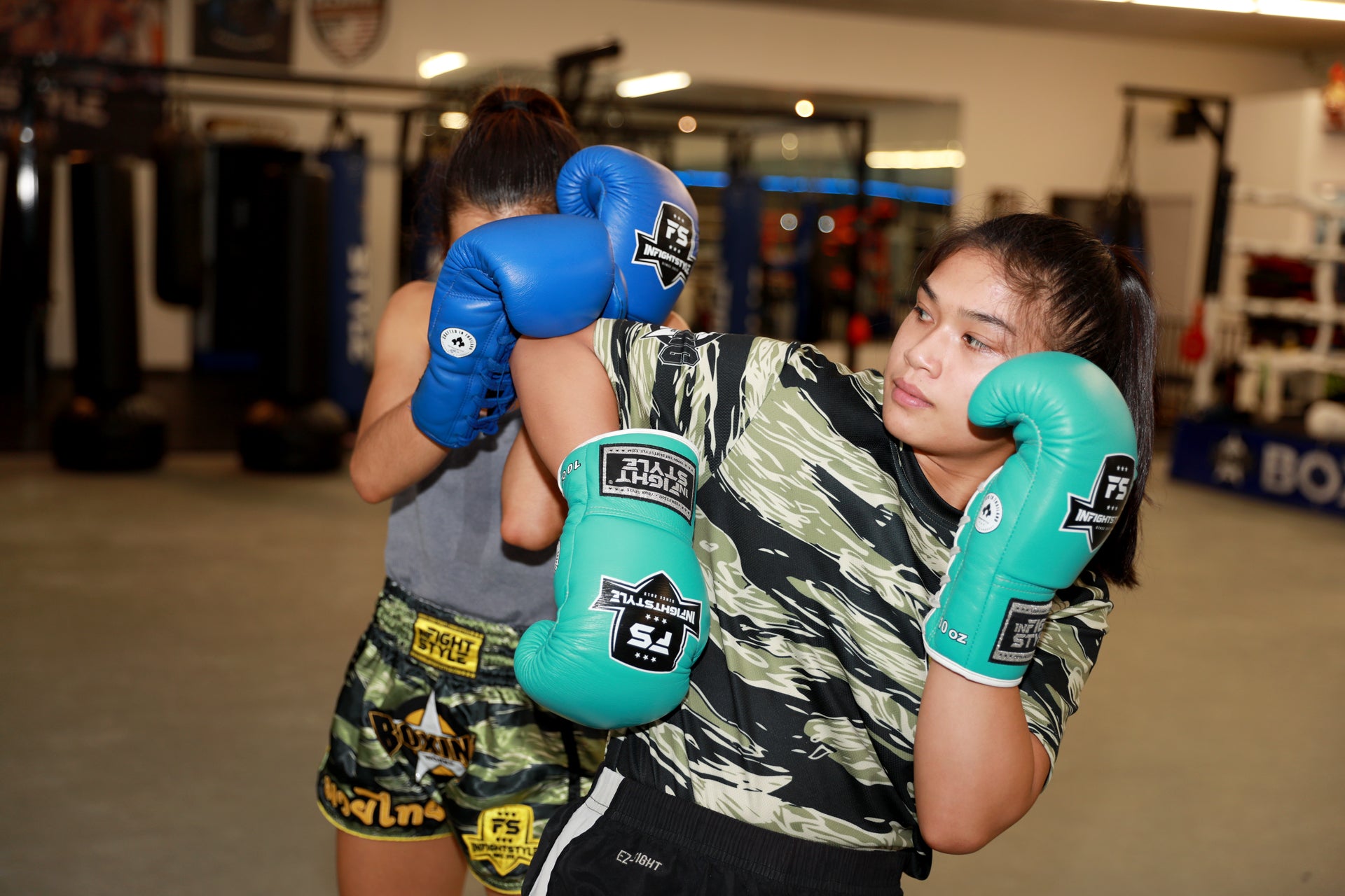 a female fighter demonstrating a spinning elbow into the guard of her training partner