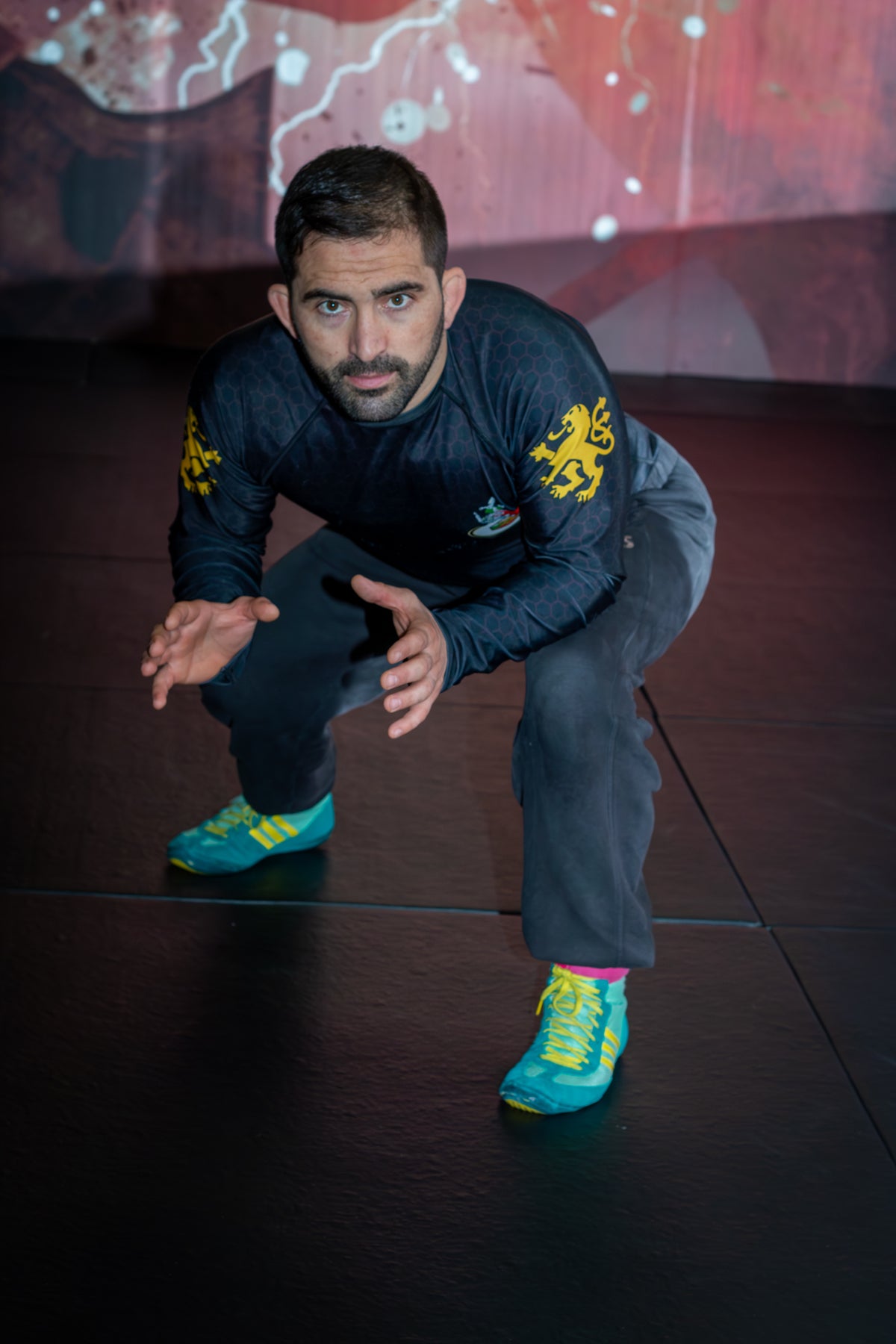 A wrestler demonstrating grappling drills with a partner on the mats in a martial arts gym
