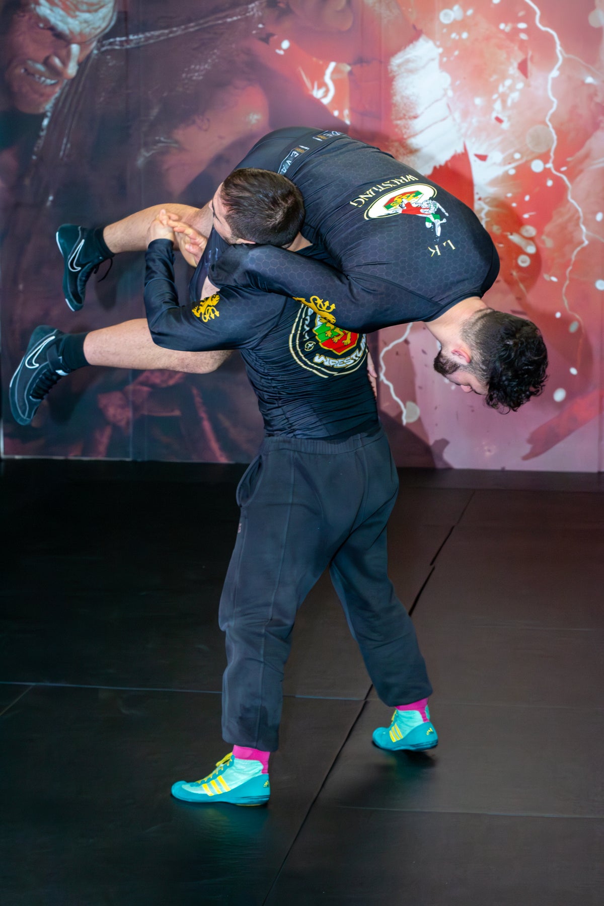 A wrestler demonstrating grappling drills with a partner on the mats in a martial arts gym