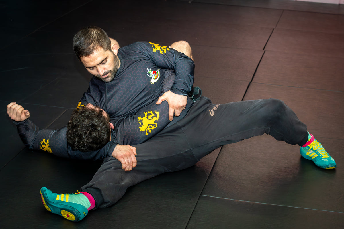 A wrestler demonstrating grappling drills with a partner on the mats in a martial arts gym